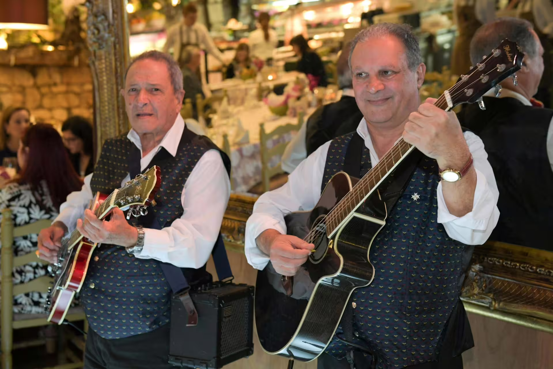 Two musicians playing guitars in traditional attire at a lively Maltese Folklore Night Tour event.