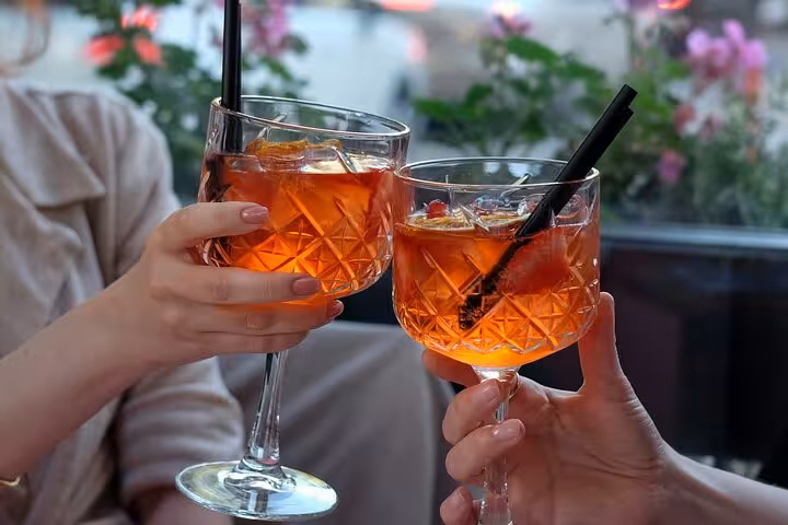 Two people toasting with Aperol Spritz cocktails on a MaMa Florence Aperitivo Tour in a vibrant setting.