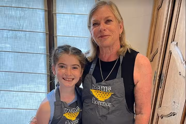 Two participants wearing Mama Florence aprons smile during the gluten-free Italian cooking class experience.