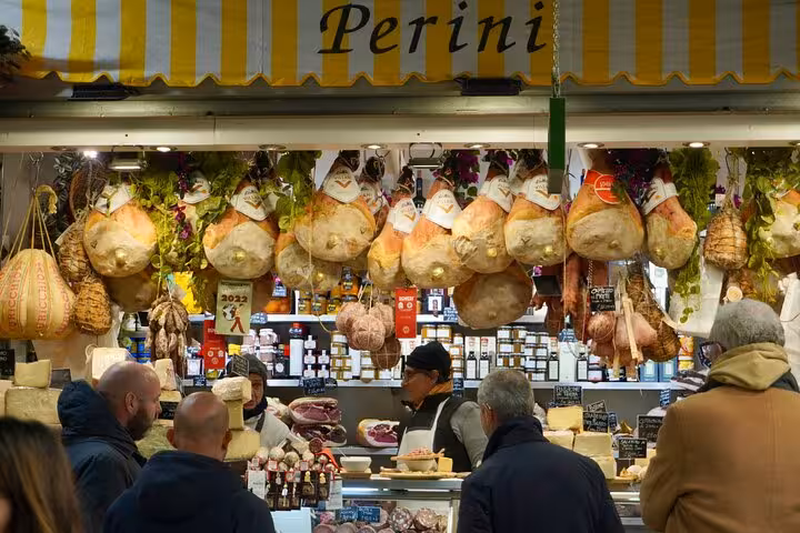 Visitors explore a vibrant Italian market stall filled with hanging cured meats during the MaMa Florence guided tour.