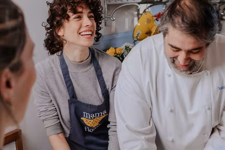 Chefs and participants smiling during a pasta cooking class at MaMa Florence in a lively kitchen setting.