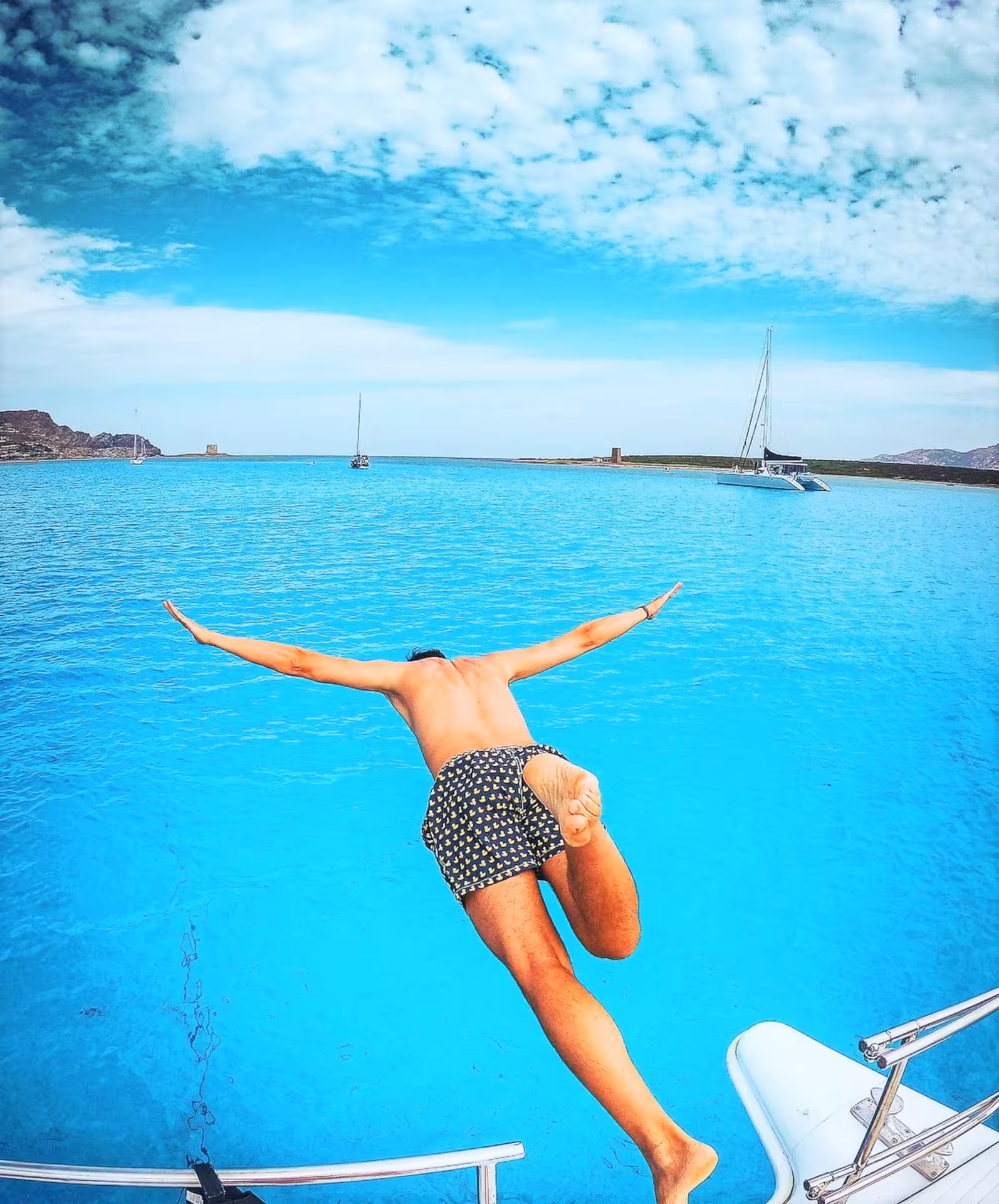 Man diving off a catamaran into the clear blue waters of the Gulf of Asinara, showcasing adventure and excitement.