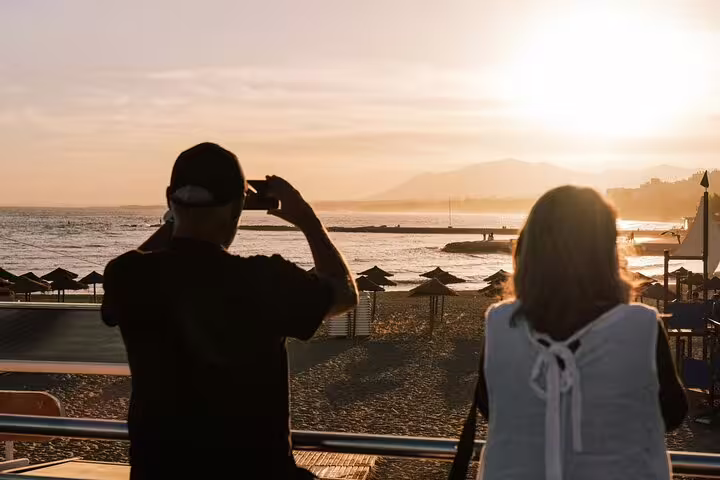 Tourists enjoy a stunning sunset view over Marbella beach, capturing the scenic moment on a private walking tour.