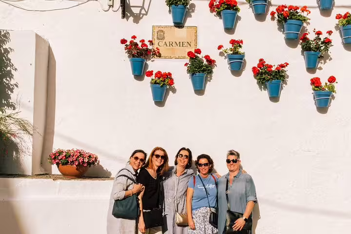 Visitors enjoy a sunny day in Marbella Old Town, posing by a charming white wall adorned with colorful flower pots.