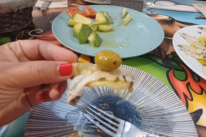 Hand holding a tapas bite with anchovy, olive, and avocado, highlighting Marbella's vibrant food tour.