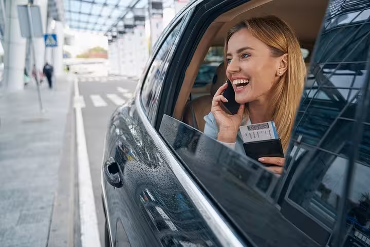 Smiling traveler in a luxury car departs Marco Polo Airport, holding passport and on phone, ready for Venice adventure.