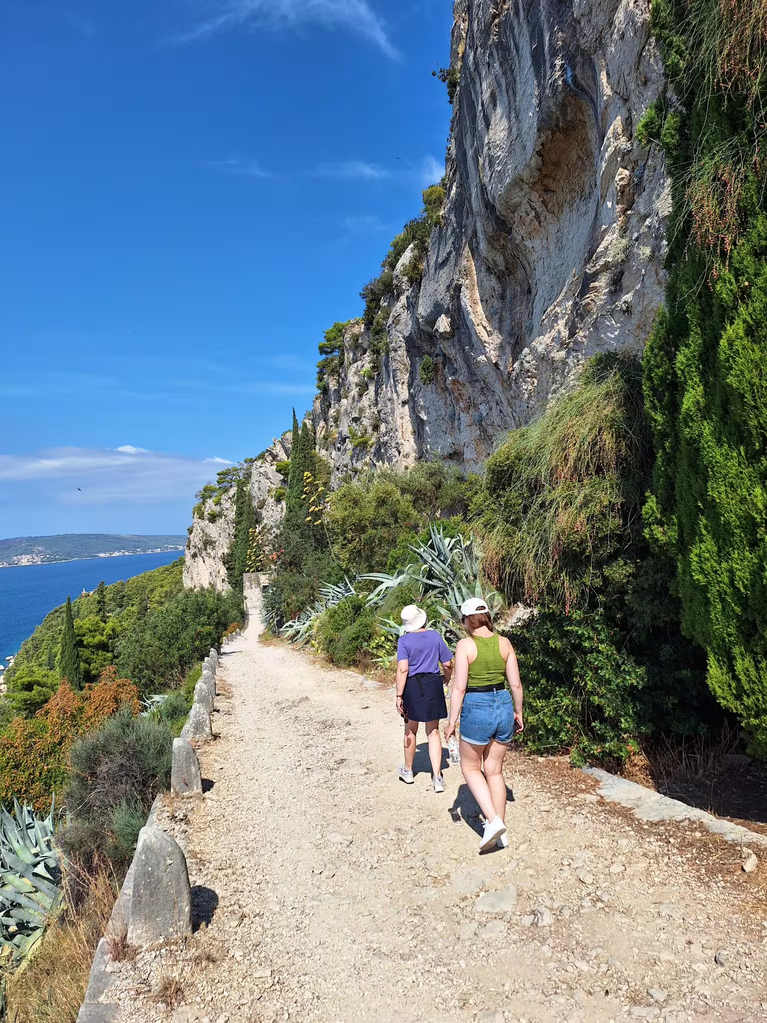 Walkers on the coastal trail beneath limestone cliffs in Marjan Park, Split, with Adriatic views on a hike