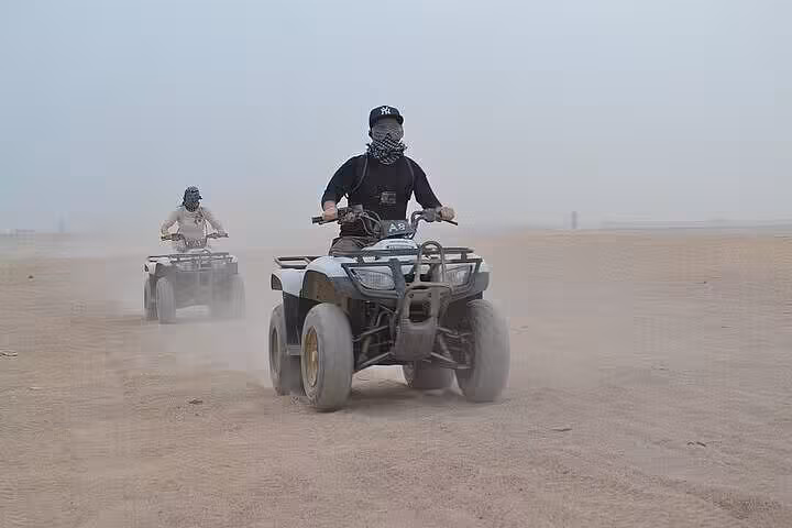 Riders on quad bikes crossing Marsa Alam desert on guided ATV safari, part of jeep and camel tour with dinner