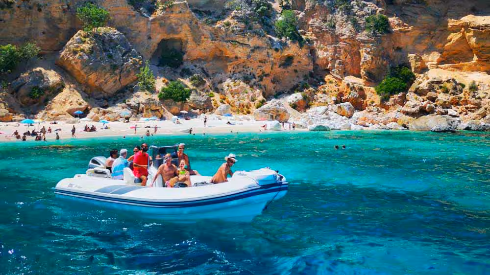 Tourists enjoy a scenic Maxi dinghy tour in the clear waters of the Gulf of Orosei near a rocky beach.