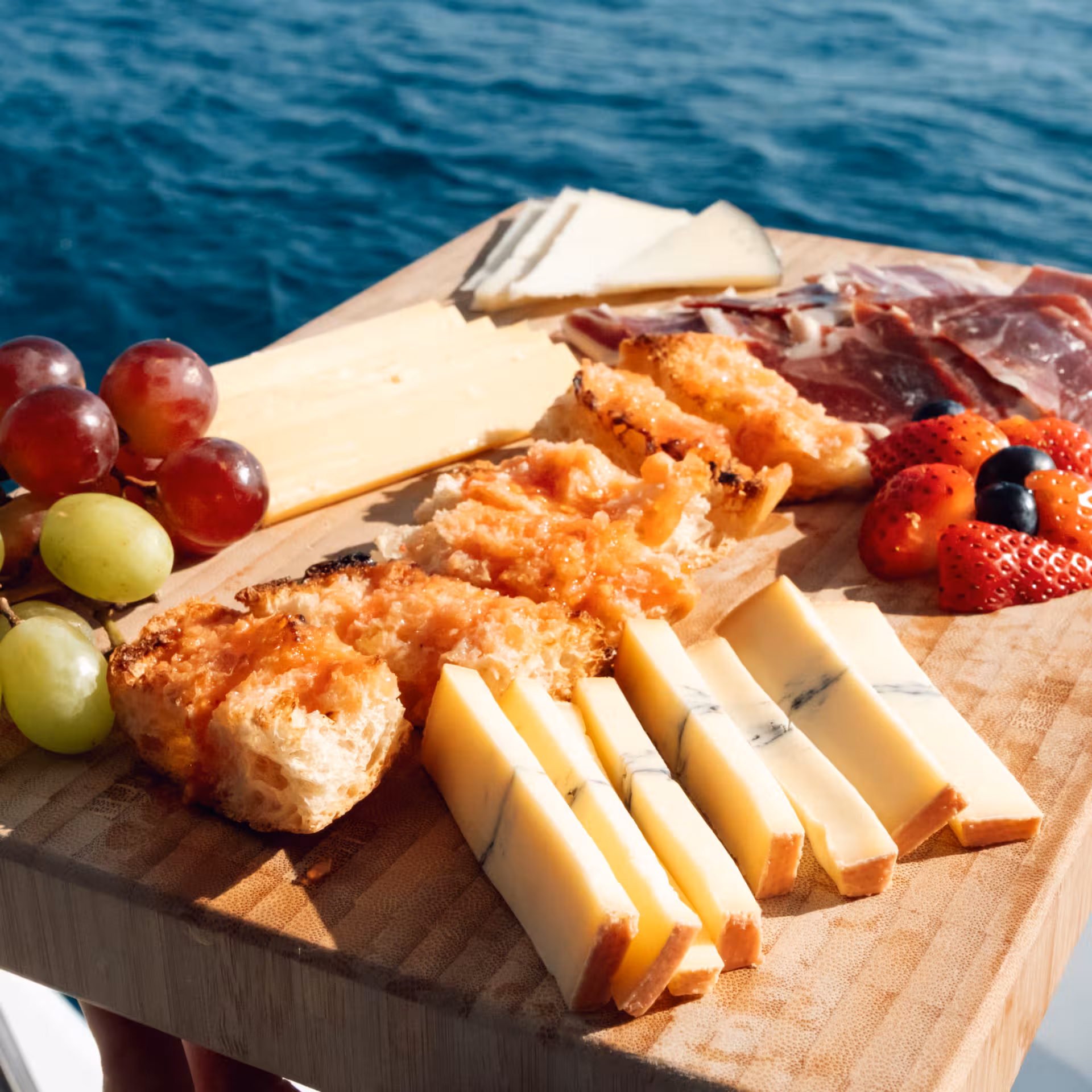 Mediterranean boat tour snack board with cheese, grapes, strawberries and cured ham served onboard after fishing