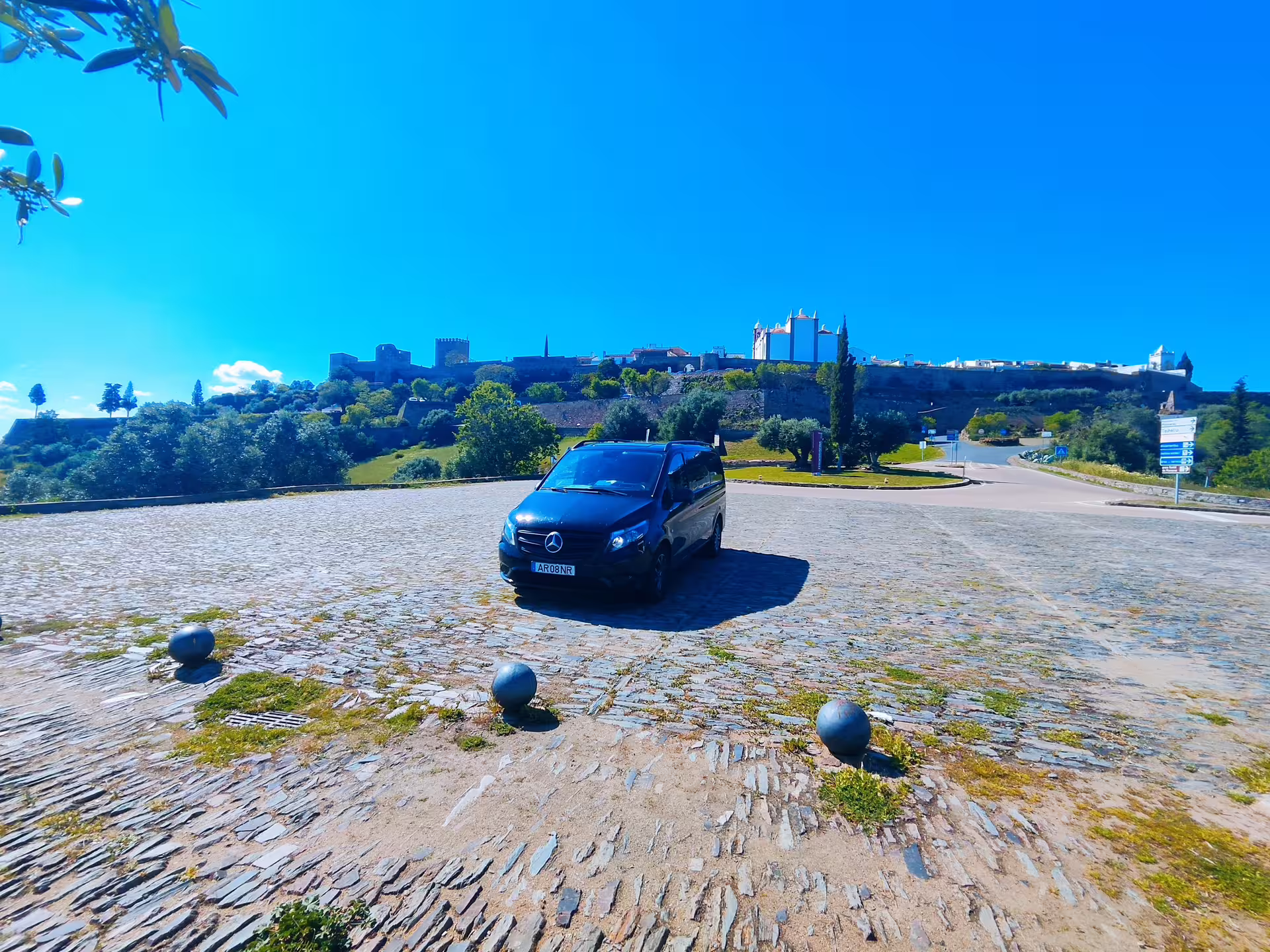Black Mercedes parked on cobbled street with scenic view of Monsaraz village under clear blue sky, Évora tour.