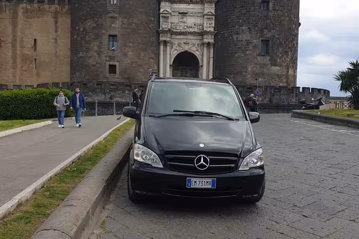 Black Mercedes van parked in front of historic Naples castle, ideal for Sorrento to Naples private transfer service.