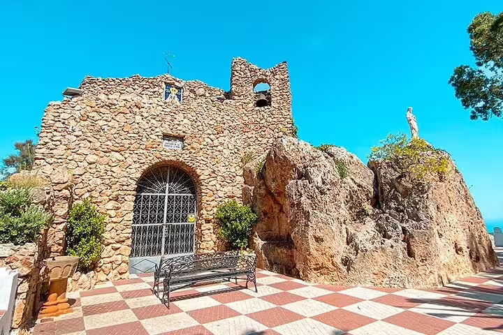 Historic stone chapel in Mijas surrounded by rocky formations under a clear blue sky, ideal for cultural exploration.
