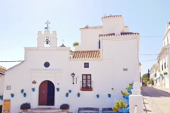 Charming whitewashed building adorned with blue flower pots, showcasing Mijas' traditional Andalusian architecture.