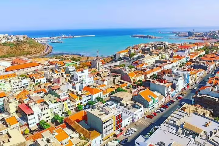 Aerial view of Mindelo, São Vicente, with colorful rooftops and vibrant harbor against a stunning ocean backdrop.