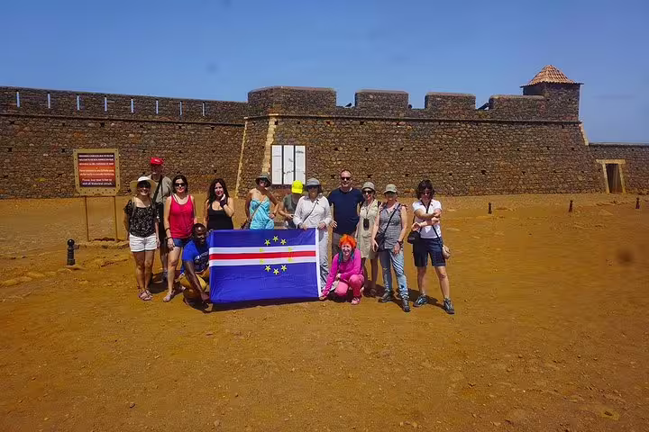 Group of tourists with Cape Verde flag at historic site in Mindelo, São Vicente Island tour.