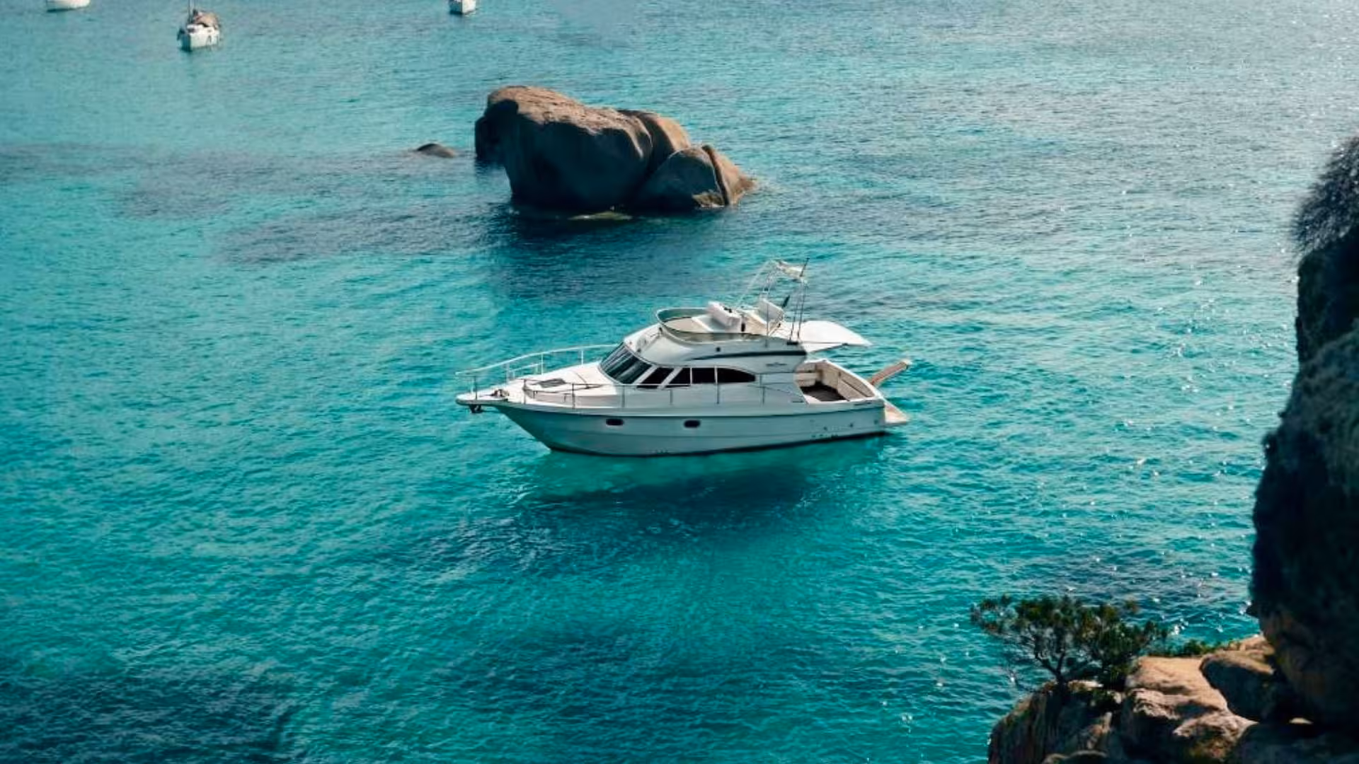 Mini yacht floating on crystal-clear turquoise waters in La Maddalena archipelago, ideal for luxury excursions.