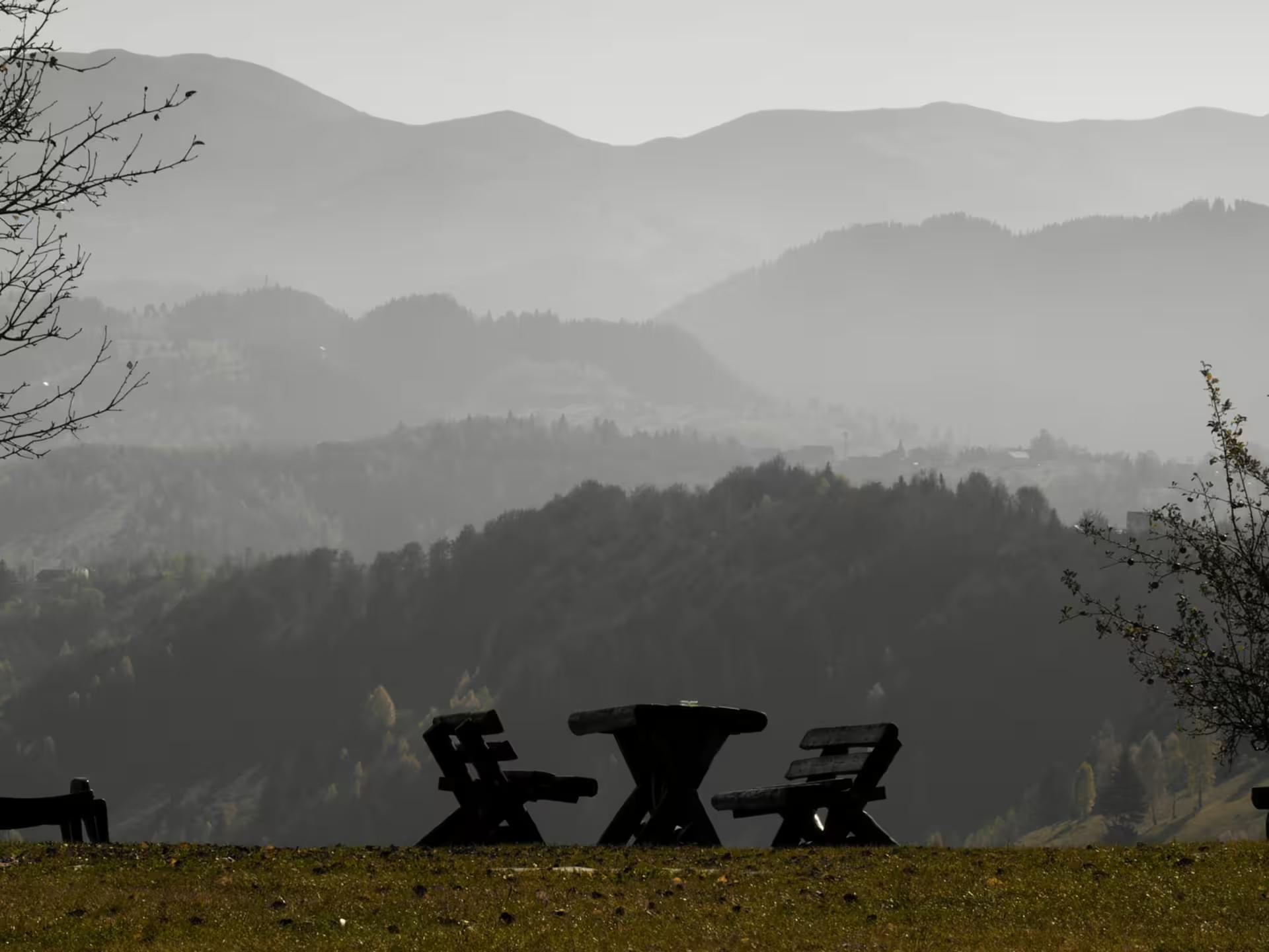 Wooden picnic table and chairs silhouetted against misty layered mountain valleys in rural Romania