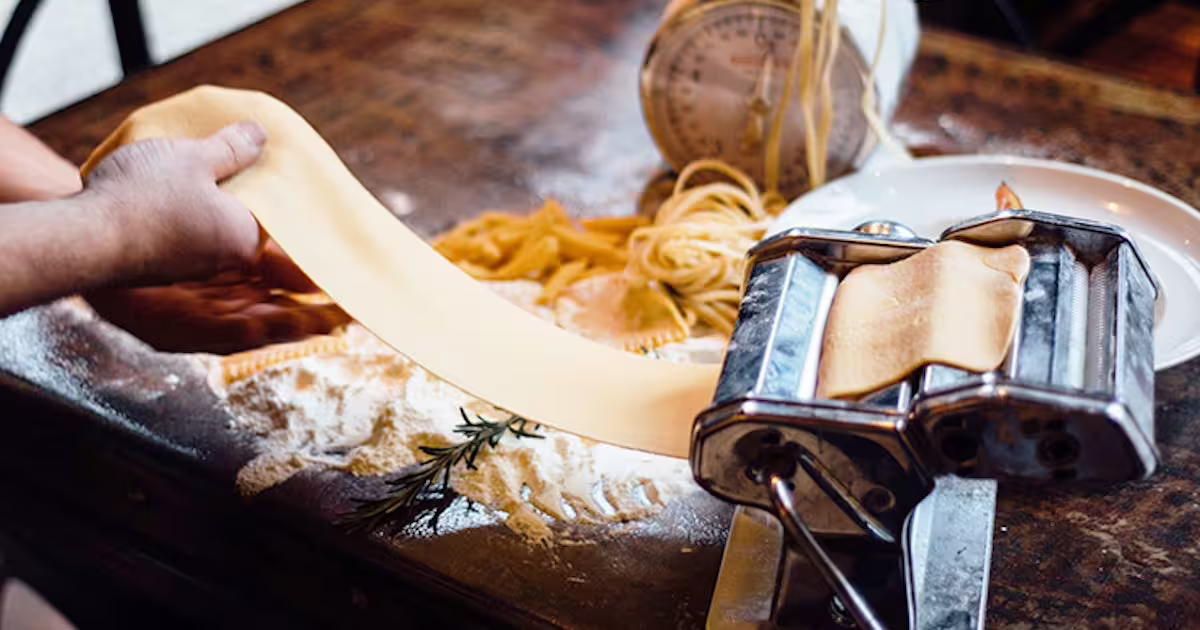 Hands rolling fresh pasta dough on a machine, a classic Modena food experience paired with balsamic vinegar tasting