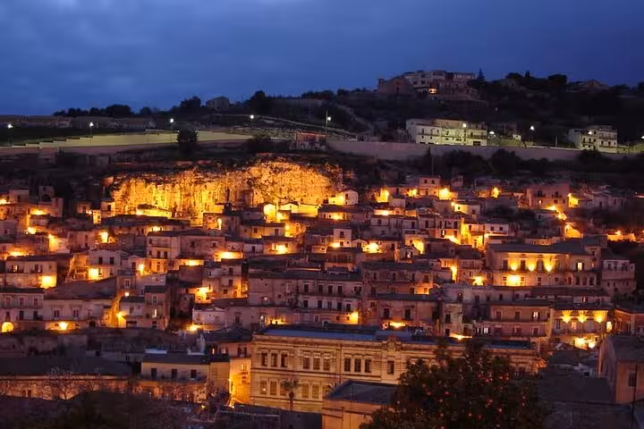 Enchanting evening view of Modica with warm lights illuminating the Baroque architecture against a dusky sky.