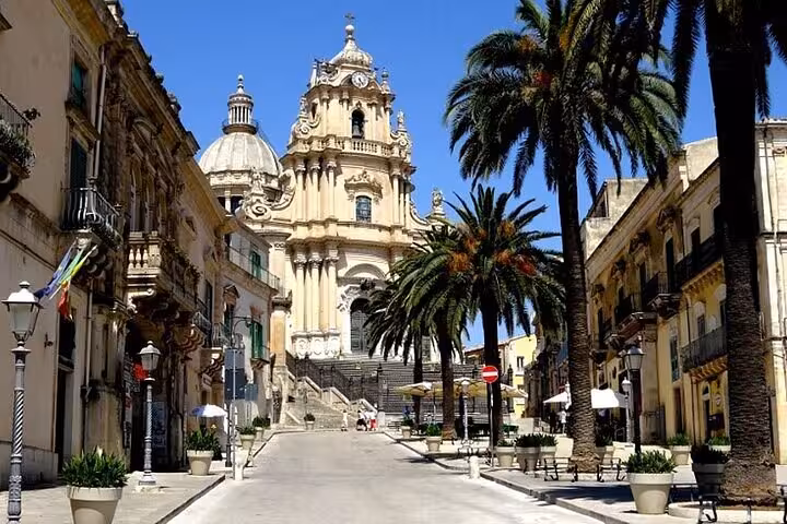 Charming street in Modica leading to an impressive Baroque church, framed by palm trees, ideal for cultural exploration.