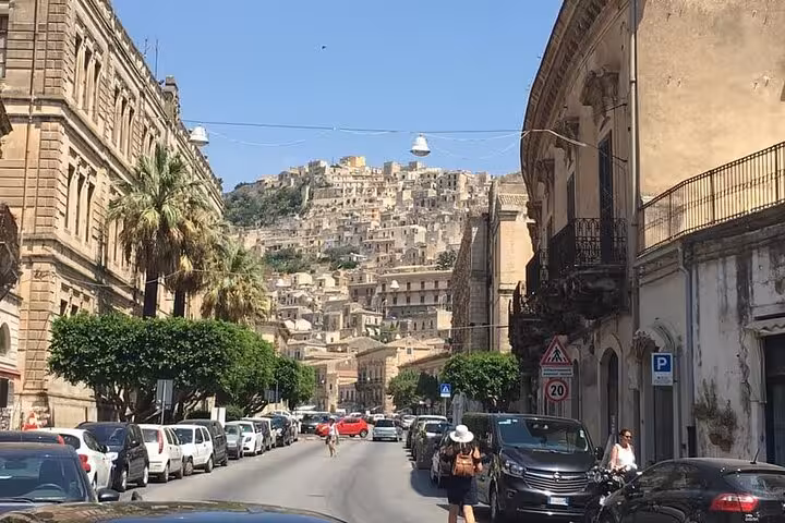Charming street view in Modica with classic Baroque buildings and a scenic hillside backdrop.