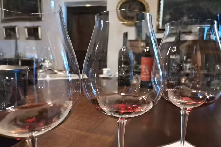 Three wine glasses with red wine residue on a wooden table during a Montalcino wine tasting tour.