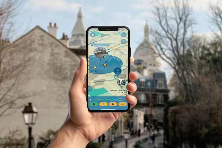 Hand holding a smartphone displaying the Montmartre self-guided GPS walking tour app with Sacré-Cœur in the background.