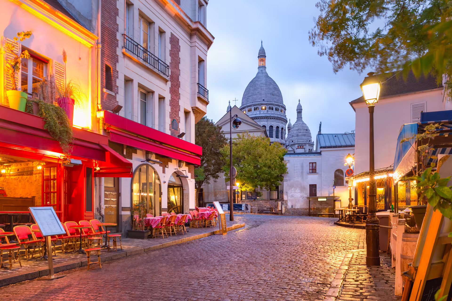 Cobblestone Montmartre street with cafés and Sacré-Cœur dome, Paris walking tour with audioguide