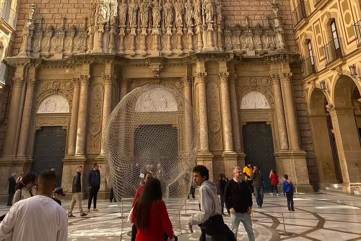 Visitors admire the intricate facade of Montserrat Basilica with ornate sculptures and a modern art installation.