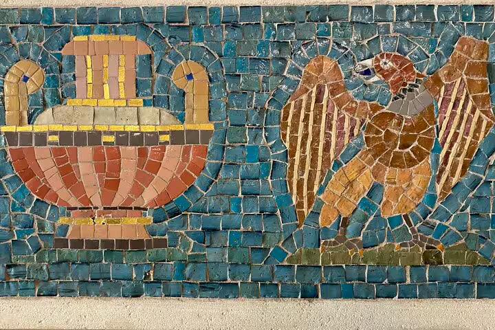 Ancient mosaic tile artwork depicting a decorative urn and eagle on turquoise background