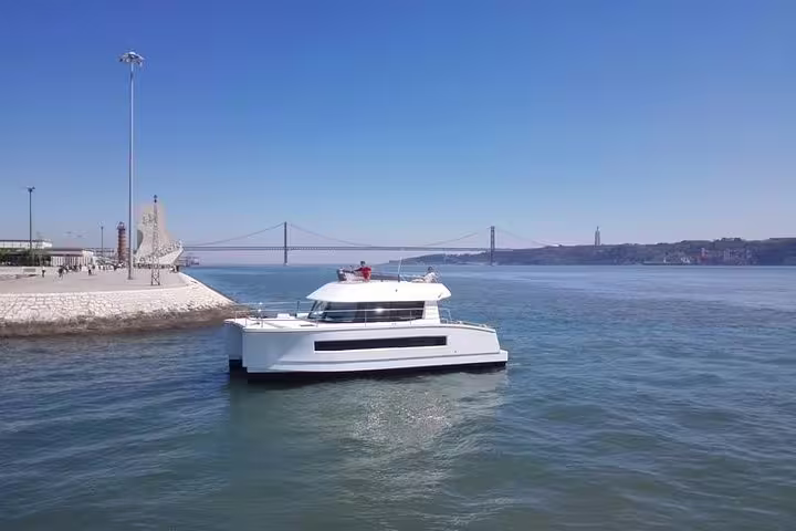 Spacious motor catamaran cruising Lisbon waters with iconic bridge and city skyline in the background.