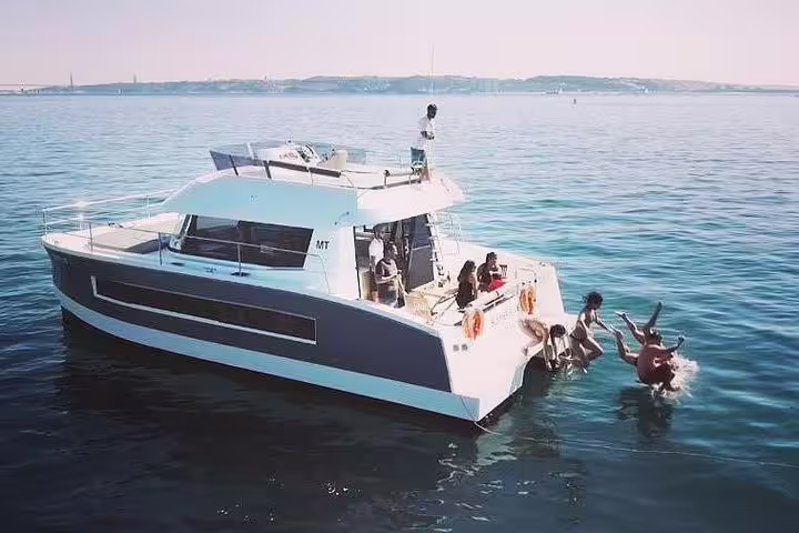 Group enjoying a swim off a motor catamaran on Lisbon's serene waters, perfect for up to 18 guests.