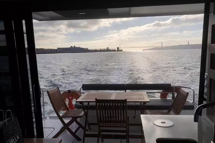 Spacious deck view of a motor catamaran with seating, sailing Lisbon's scenic waters at sunset.