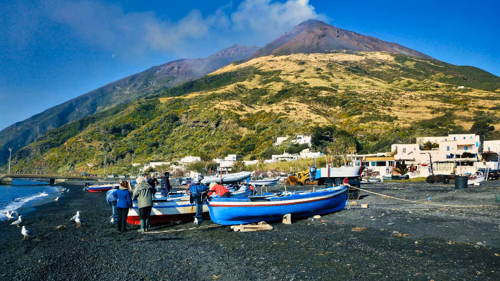 Vibrant motorboats on Stromboli's black sand beach with smoking volcano backdrop, perfect for Aeolian Islands tours.