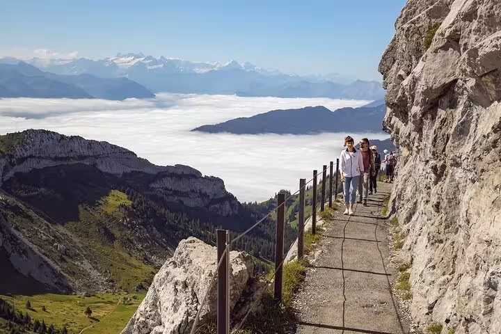 Hikers enjoy a scenic trail on Mount Pilatus with panoramic views over clouds and the Swiss Alps.