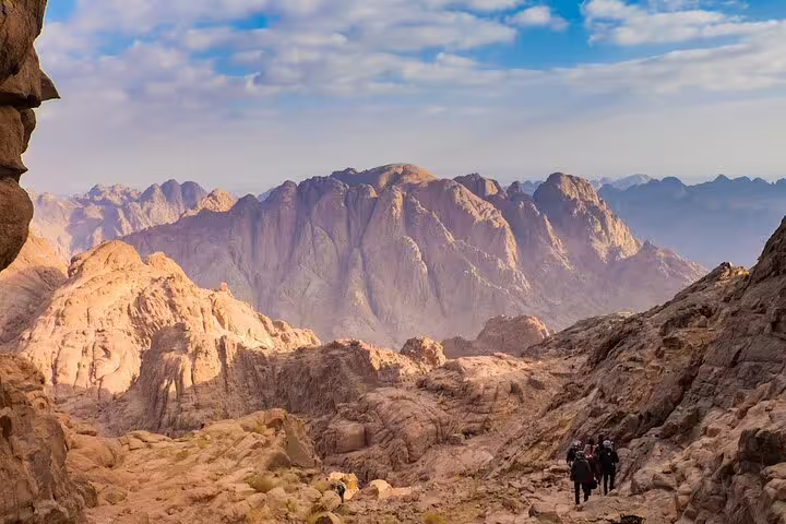 Hikers ascending Mount Sinai trail at sunrise on a Dahab tour, with panoramic Sinai mountains and desert views