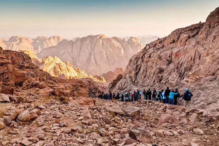 Group trekking rocky Mount Sinai trail at sunrise on Dahab to Saint Catherine Monastery and summit hike