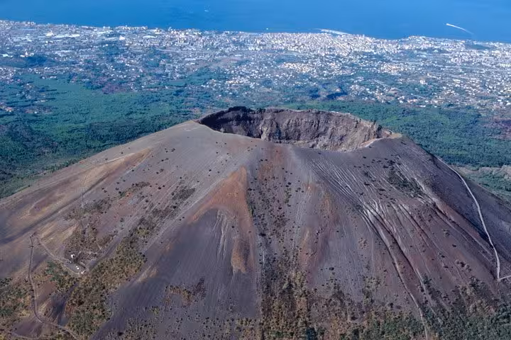 Aerial view of Mt. Vesuvius crater with the stunning backdrop of Naples and the coastline, ideal for day-trip exploration.