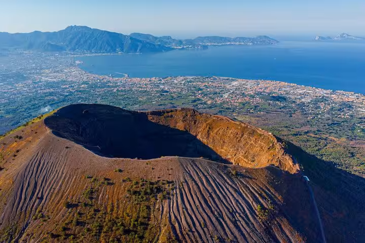 Aerial view of Mount Vesuvius crater with Naples coastline in the background, perfect for Pompeii day tours.