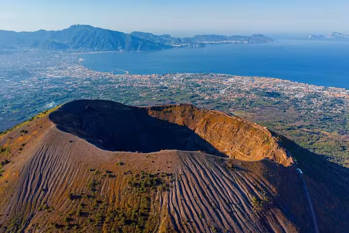 Aerial view of Mount Vesuvius crater with stunning Naples coastline backdrop, ideal for Amalfi Coast tours.