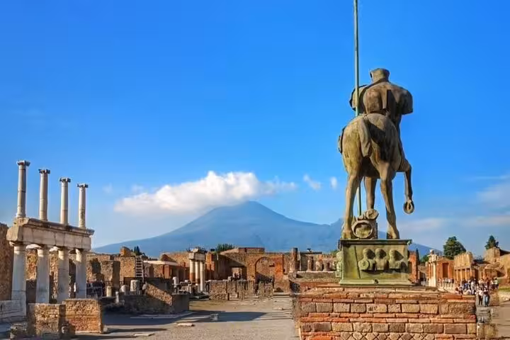 View of Mount Vesuvius from Pompeii with ancient ruins and a prominent statue in the foreground.