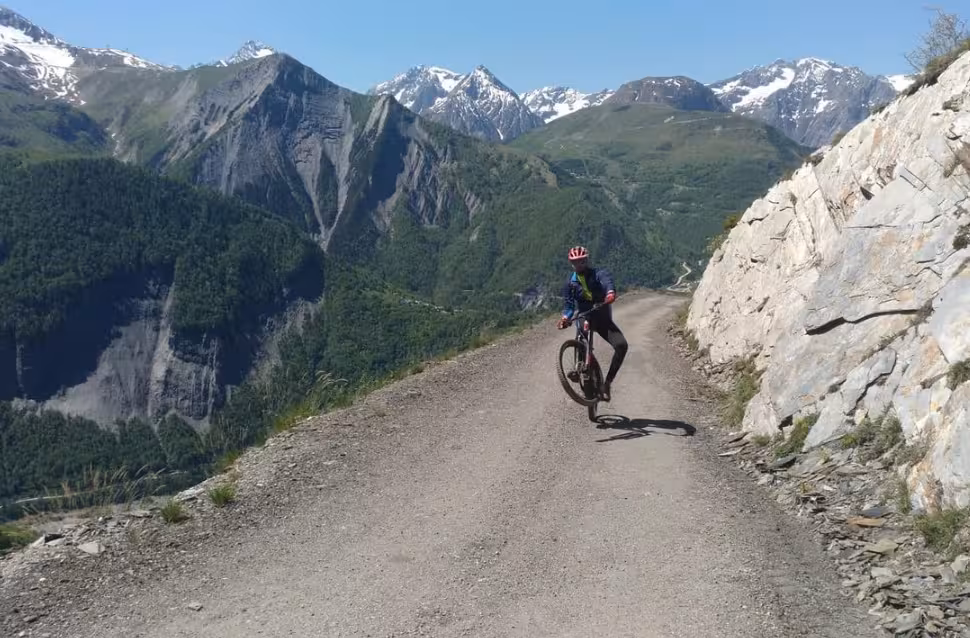 Cycliste en VTT sur route de montagne avec sommets enneigés, tour aventure rouler sur la neige