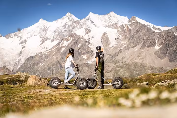 Two riders on mountain scooters with snowy peaks, Swiss Alps adventure from Zurich Airport to Jungfrau region
