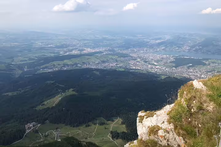 Panoramic view from Mt. Pilatus summit, overlooking Lucerne's sprawling landscape and shimmering lake under a clear sky.