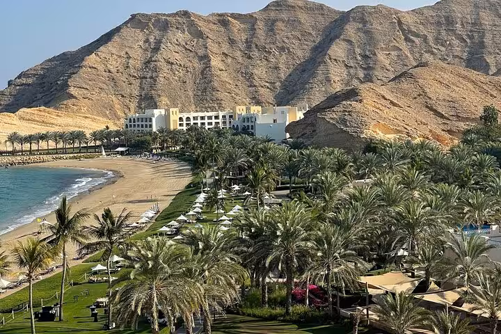 Scenic Muscat beachfront resort with palm trees and mountains, ideal drop-off point for private chauffeur transport service