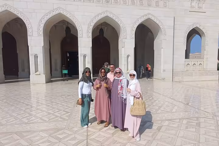Group of women in modest dress posing in the marble courtyard of Sultan Qaboos Grand Mosque on a Muscat City half-day tour