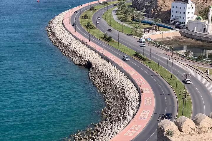 Scenic coastal road with palm trees and turquoise waters seen on an Omani-guided morning tour in Muscat.