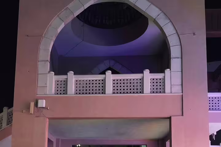 Elegant archway and balcony with intricate designs illuminated at night in Muscat, showcasing traditional Omani architecture.