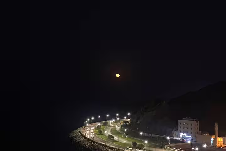 Full moon over Muscat's coastal road, with streetlights illuminating the scenic evening landscape for a private tour.